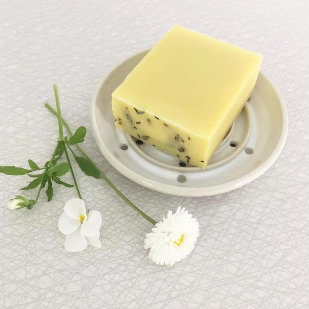 Naturlig handgjord tvål med örter på ett elegant vitt tvålfat, stylat med vita fräscha blommor- perfekt för hudvård och ekologisk livsstil.