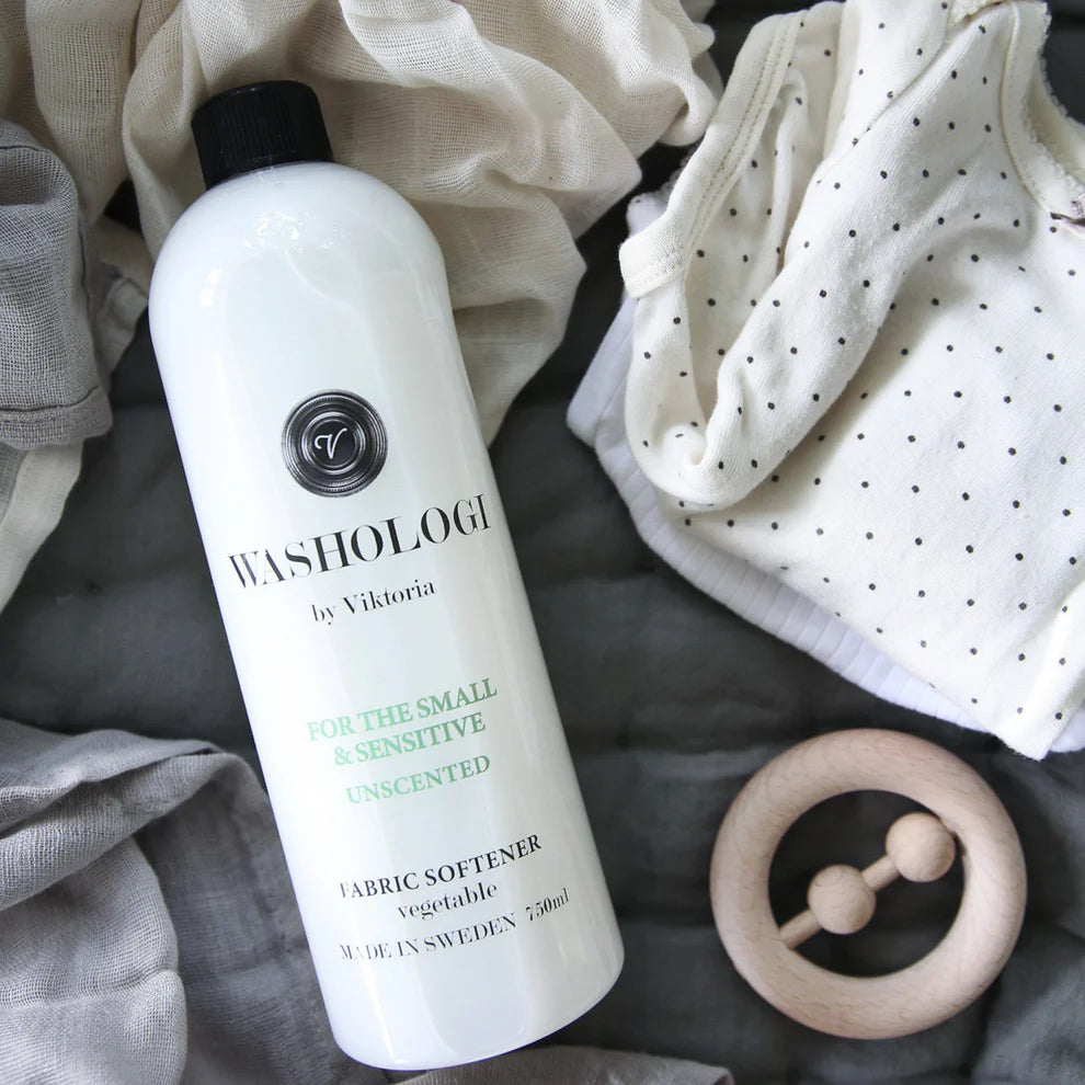 Miljövänligt och oparfymerat mjukmedel från Washologi, skonsamt för känslig hud och barnkläder, fotograferat tillsammans med ljusa textilier och babyaccessoarer